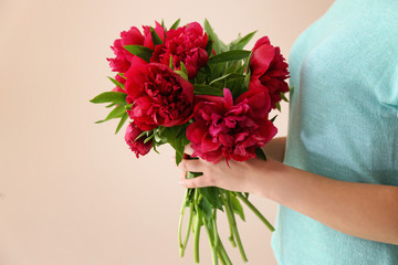 Young woman holding bunch of peonies on color background
