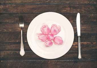 Pink tulips heads over plate on wooden table. Top view with copy space. Diet or vegan concept.