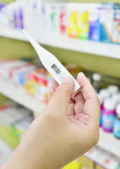 Hand holding digital thermometer at the pharmacy on blur medicines for children shelves.
