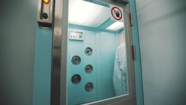 Scientist in sterile white robe clothes blue rubber gloves walks out disinfection chamber at serious radioactive danger laboratory