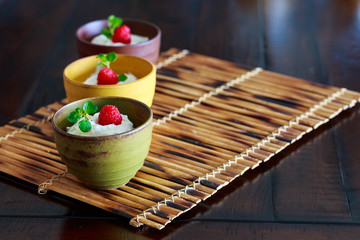 3 Greek yogurts with blueberry and raspberry in colorful Japanese bowl on bamboo mat.