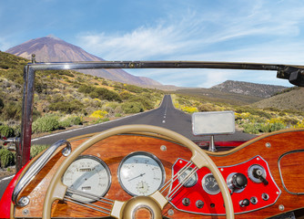A view from behind the steering wheel of a vintage convertible driving on a mountain road