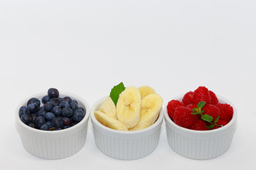blueberry, raspberry and banana in the ramekins  on white background.