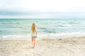 Young blonde girl standing on the beach