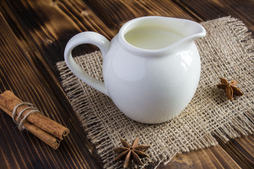 Milk in the ceramic jug with cinnamon on the wooden background