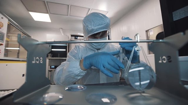 Scientist caucasian man in sterile clothes, face mask and rubber gloves puts magnifier lenses on special metal holder at laboratory