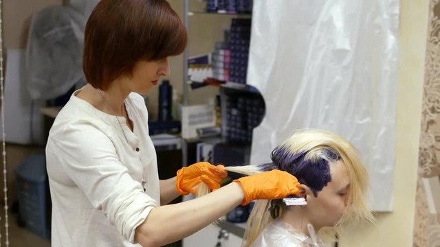 Hair-stylist makes hair color, blonde, dyes hair in blue.