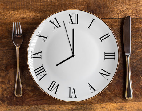 Eight hour feeding window concept or breakfast time with clock on plate and knife and fork on wooden table, overhead view