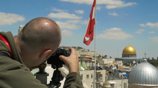 Photographer is taking picture of rooftops of Old City of Jerusalem. A view on Grey dome of Church and golden Dome of the Rock.