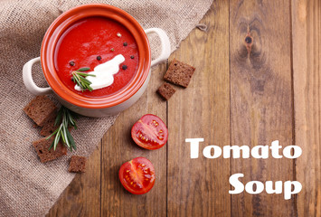 Pot of tasty tomato soup and ingredients on wooden background