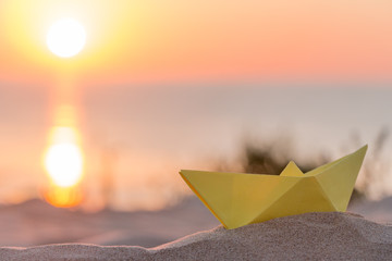 Yellow paper boat on a beach at sunrise