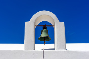 Obraz premium White church tower with bell against blue sky background near Paleochori Beach, Milos island, Greece
