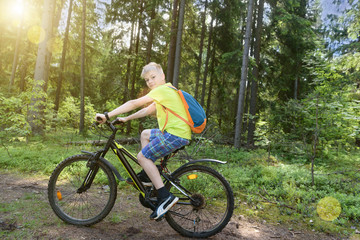 Fototapeta na wymiar Happy teenager rides a bicycle in pine wood, in sunny day.
