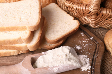 Composition of sliced bread and scoop with flour on cutting board