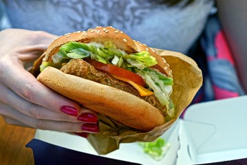 Гамбургер из курицы салата томатов и сыра в руке