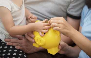 Asian little kid girl putting coin into yellow  piggy bank with family.