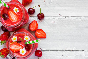 strawberry and cherry smoothie in glass jar with a straw and fresh fruits and berries