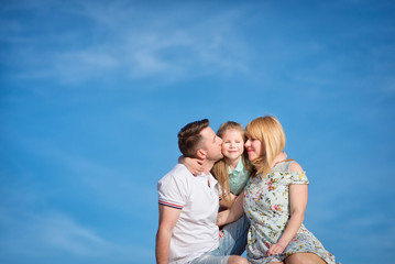 Happy beautiful laughing family sitting on the sand on the beach against the background blue sky in summer vacation.