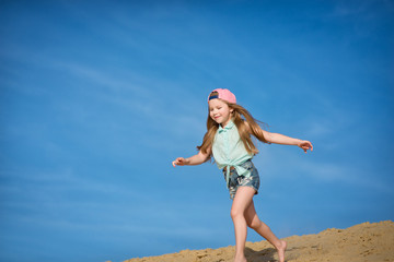 Little active girl  walking, running, jumping, having fun along the sand on the beach against the background blue sky in summer vacation.