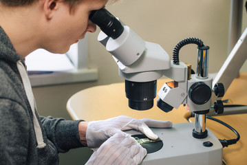 Young man repairing computer components in service center using microscope. Electronics repair and fix service concept.