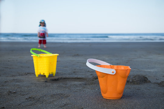 A pair of toy buckets at the beach with a child in the background