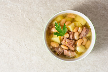 Beef soup with potatoes, beans and leeks in ceramic bowl on stone background.