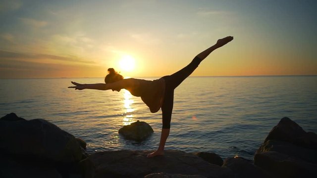 Healthy young flexible girl practice yoga asanas sea coast sunrise slow motion