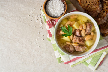 Beef soup with potatoes, beans and leeks in ceramic bowl on stone background.