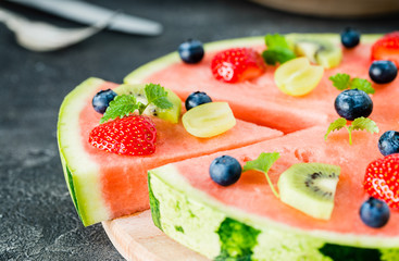 Watermelon pizza cut with fruits on wooden board, close up
