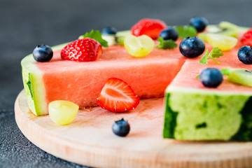 Watermelon pizza cut with fruits on wooden board, close up