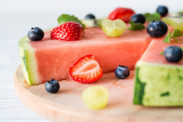 Watermelon pizza cut with fruits on wooden board, close up