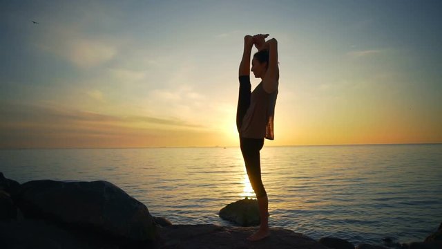 Healthy young flexible woman doing yoga asanas sea coast sunrise slow motion