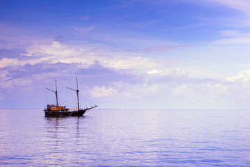 Wooden sailboat, or pinici, in vast Indian ocean under cloudy sky on sunrise, Indonesia. Seascape for wallpaper or background.