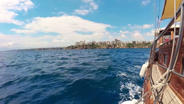 The Mediterranean sea, picturesque coast town, a wooden boat - yacht floating on the waves, view of the ship. summer sun, blue sky, azure water. Spray and foam. Antalya, Turkey. Video stabilization
