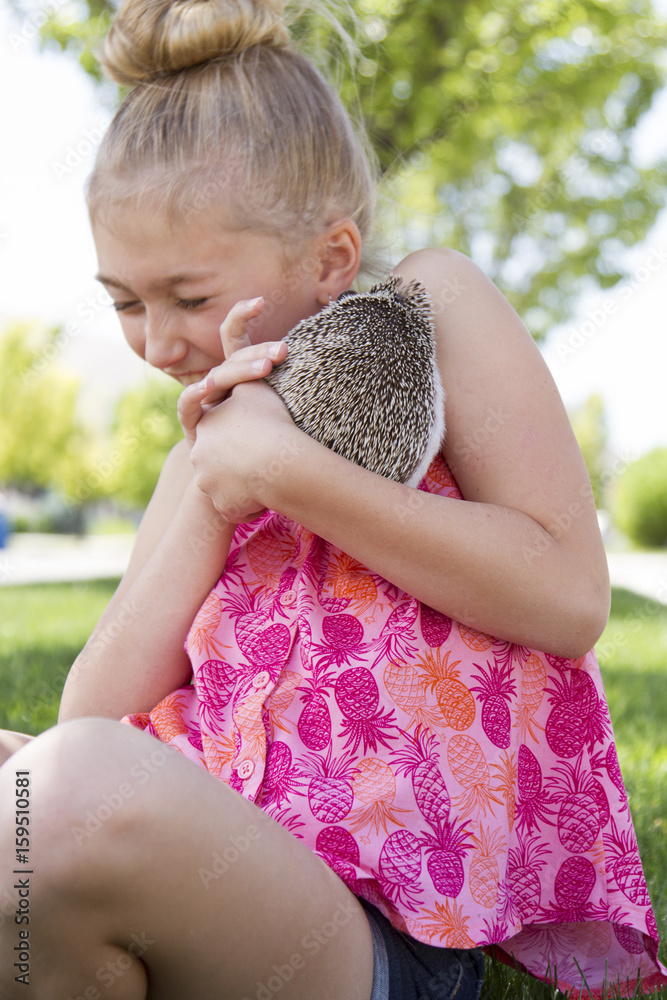 Wall mural Young girl holding a pet hedgehog outside