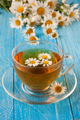 Herbal tea with fresh chamomile flowers on blue wooden background