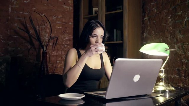 Girl drinking coffee while working on her laptop at night
