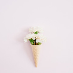 Waffle cone with white carnation bouquet on pale pastel pink background. Flat lay, top view