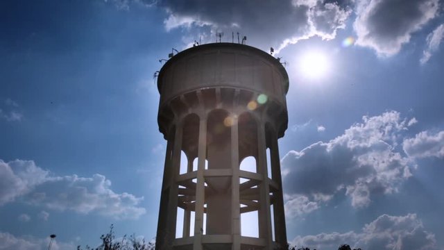 Northcliff JHB - Center placement - Looking up at a large concrete reservoir on stilts with arches the water tower against cloudy background with lens flare sun