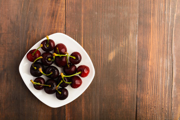 Many healthy cherries on white plate over brown wooden background