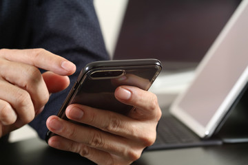 close up of businessman hand working with smart phone and laptop and digital tablet computer in modern office