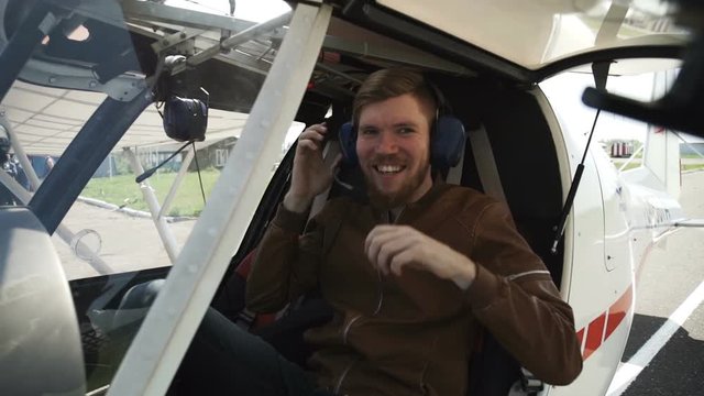 The pilot is in the cabin of a small plane. In headphones and a brown leather jacket, with a red beard.