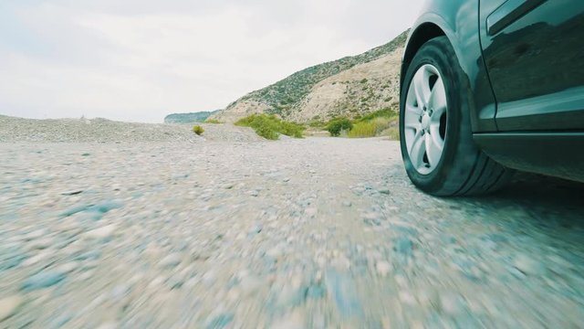 Wheels of the car are moving along a dirt road, In the background high mountains. Overcast summer weather, Light, airy clouds. Auto rides on a dirt road. View from on-board camera on weel and wing