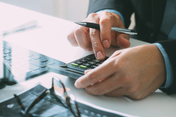close up of businessman hand working with finances about cost and calculator and latop with mobile phone on withe desk in modern office - obrazy, fototapety, plakaty