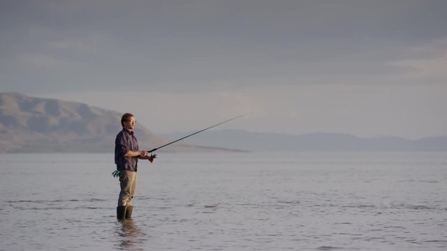 Wide panning shot of man watching fly fishing at lake. Vineyard, Utah, United States