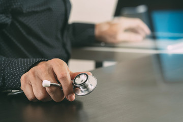 close up of smart medical doctor working with stethoscope and laptop computer on dark wooden desk