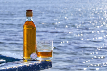 Bottle with glass whiskey and watch on background of lake