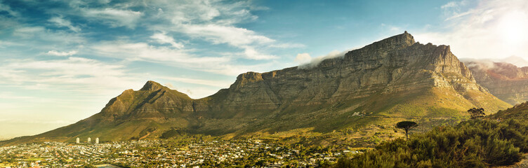 Breathtaking landscape panorama of table mountain, in cape town, south africa, with dramatic clouds and warm sunlight casting a shadow from the mountain over the city.