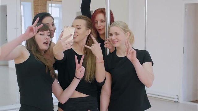 Group of beautiful young women taking a selfie with smartphone during a pole dance class