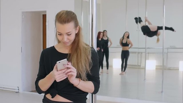 Cute pole dancer using cell phone during a pole dance class